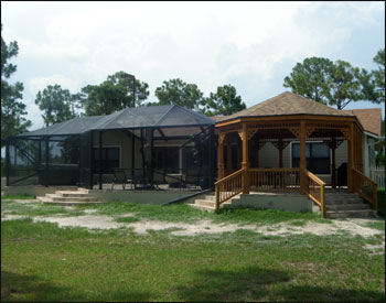 16x22 Treated Pine Custom Gazebo shown with One Rectangular Hip End and One Oval Hip End, No Floor, 2x2 Decorative Spindle Railings, Decorative Braces,  Taller Posts, 36” Post Trim, Rustic Cedar Asphalt Shingles, Two Coats Cedar Toned Stain and Sealer, and Hurricane Package